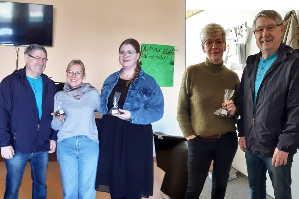 Vier Personen posieren in einem Innenraum mit kleinen Troph&auml;en in der Hand.