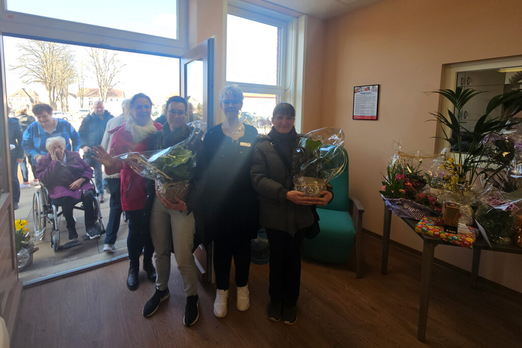 Menschen stehen in einem Raum mit Blumenstr&auml;u&szlig;en.