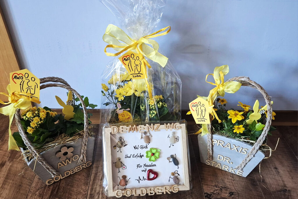 Drei Blumengestecke mit AWO-Karten und Gl&uuml;ckwunschtafel