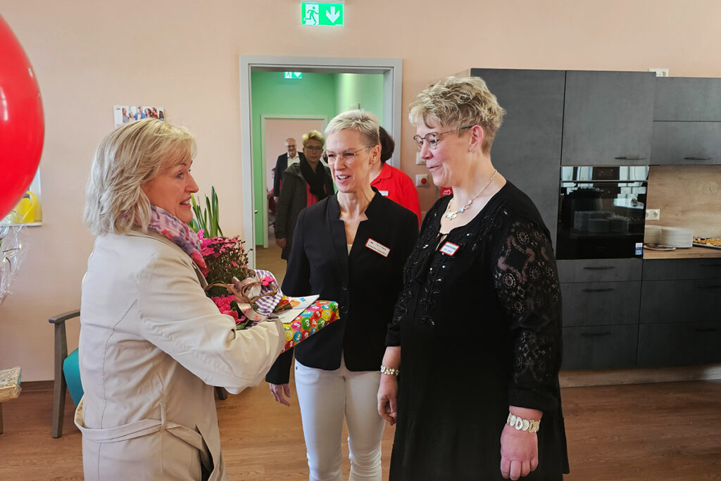 Eine Frau &uuml;bergibt ein Geschenk an zwei andere Frauen in einem Innenraum.