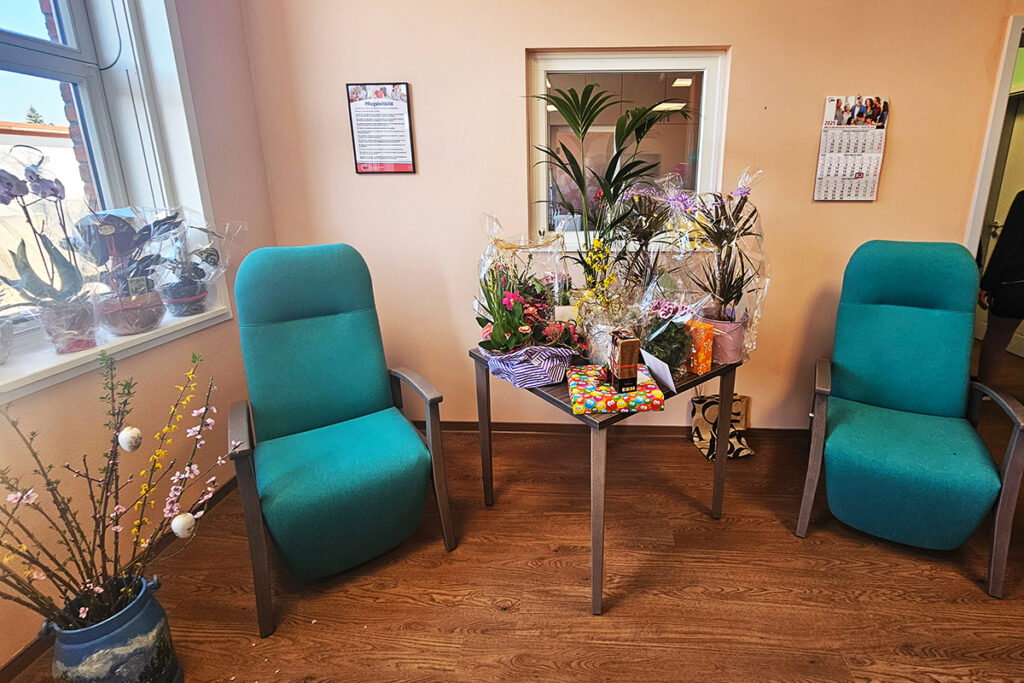 Innenraum mit zwei gr&uuml;nen St&uuml;hlen, einem Tisch mit Pflanzen und Geschenken, und Dekoration auf einem Holzfu&szlig;boden