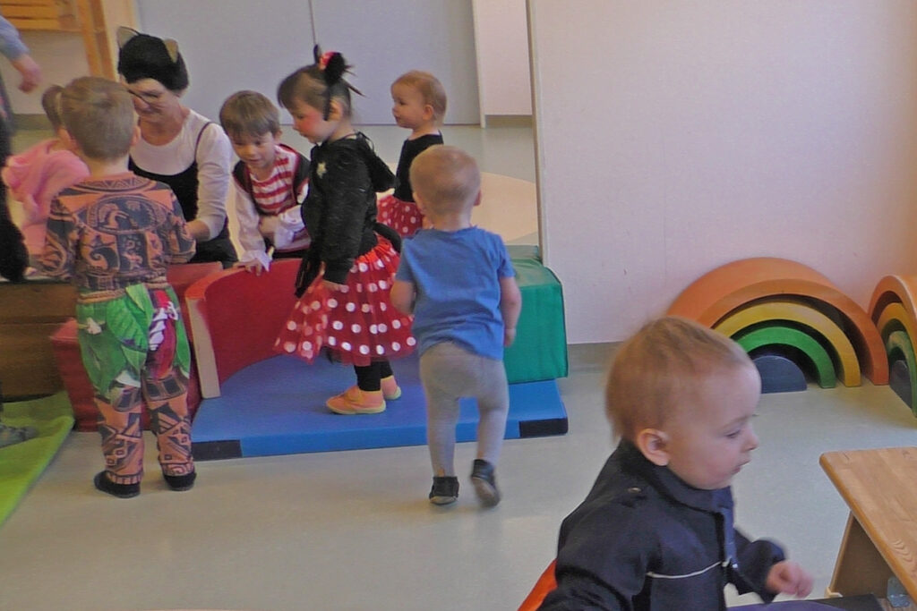 Kinder spielen in einem Innenraum mit bunten Schaumstoffelementen und eine Frau schaut zu.