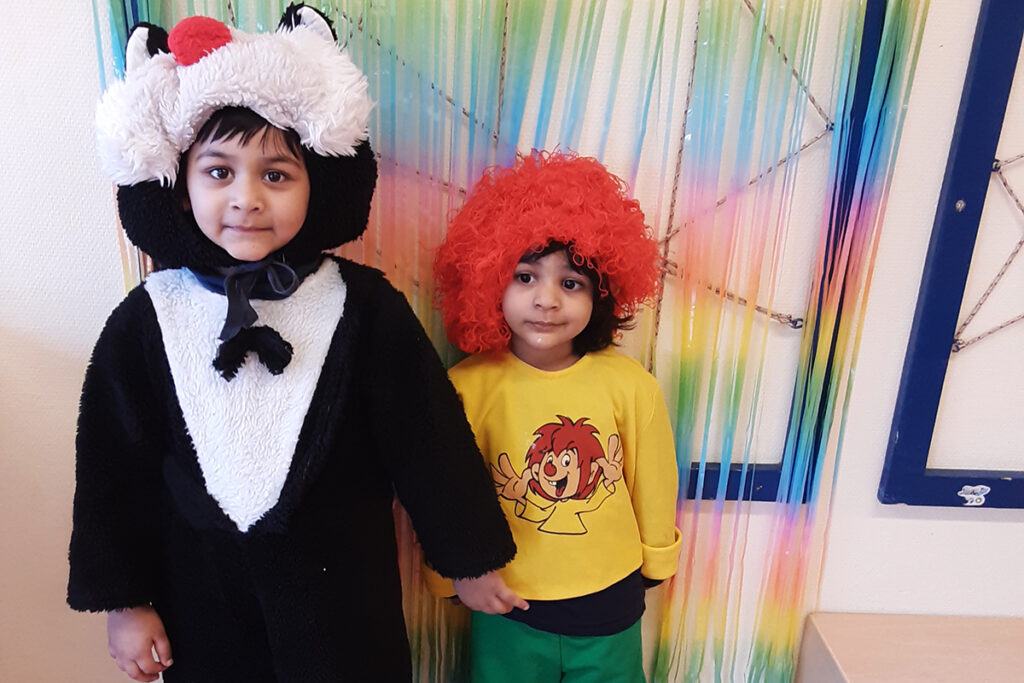 Zwei Kinder in Kost&uuml;men vor einem bunten Hintergrund.