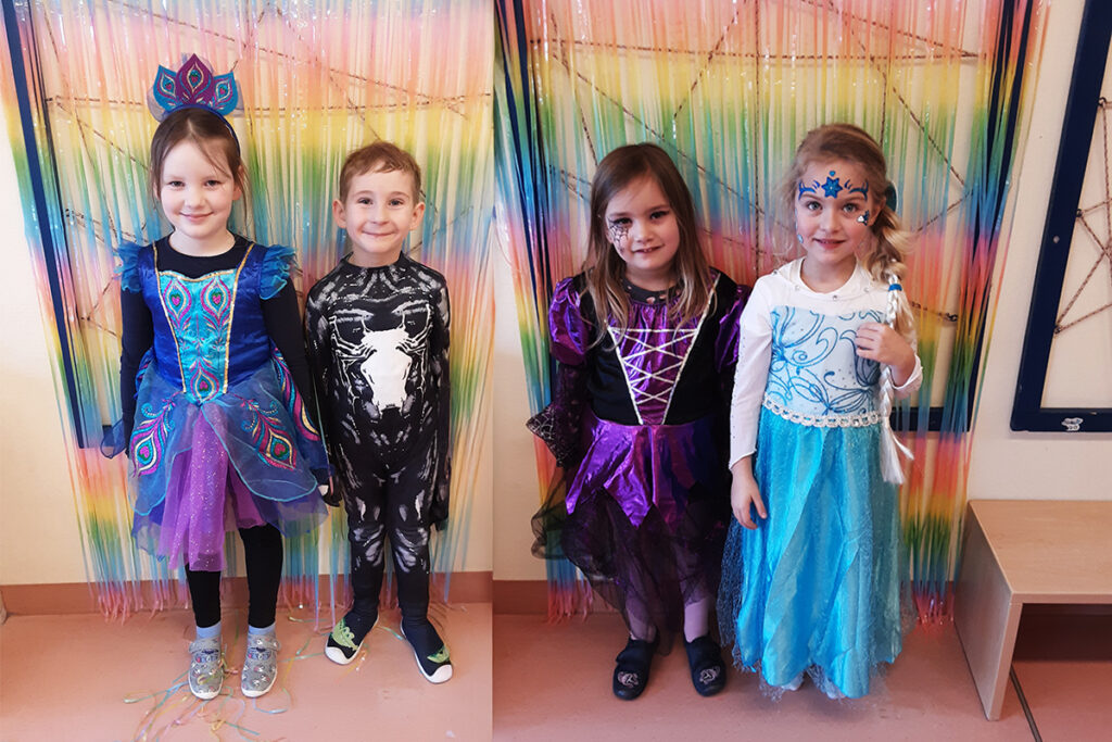 Vier Kinder in bunten Kost&uuml;men vor einem regenbogenfarbenen Hintergrund