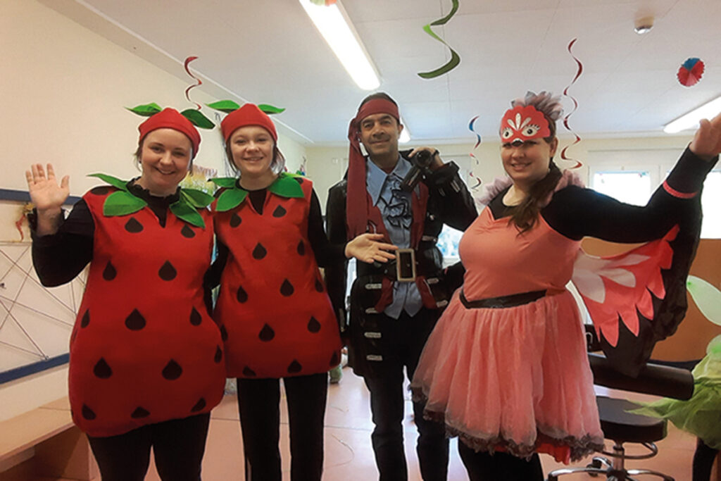 Vier Personen in verschiedenen bunten Kost&uuml;men posieren fr&ouml;hlich in einem Raum mit Partydekoration.