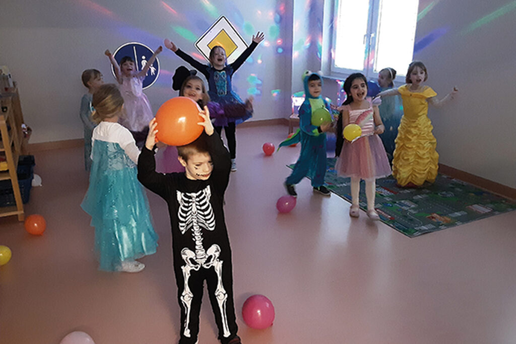 Kinder in Kost&uuml;men feiern mit Luftballons in einem Raum.