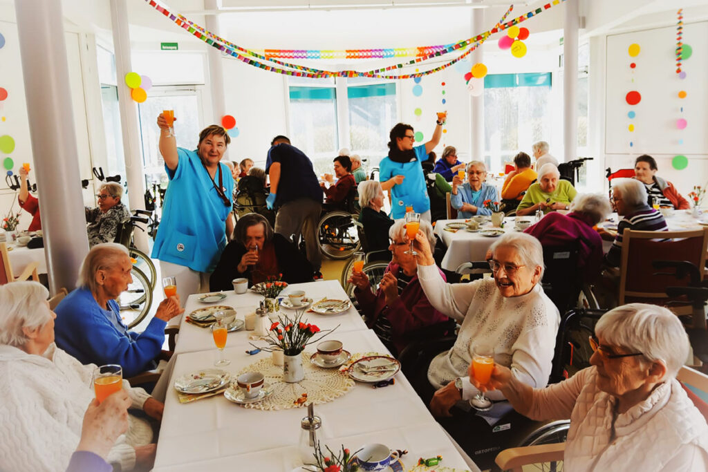&Auml;ltere Menschen und Betreuer feiern in einem Gemeinschaftsraum