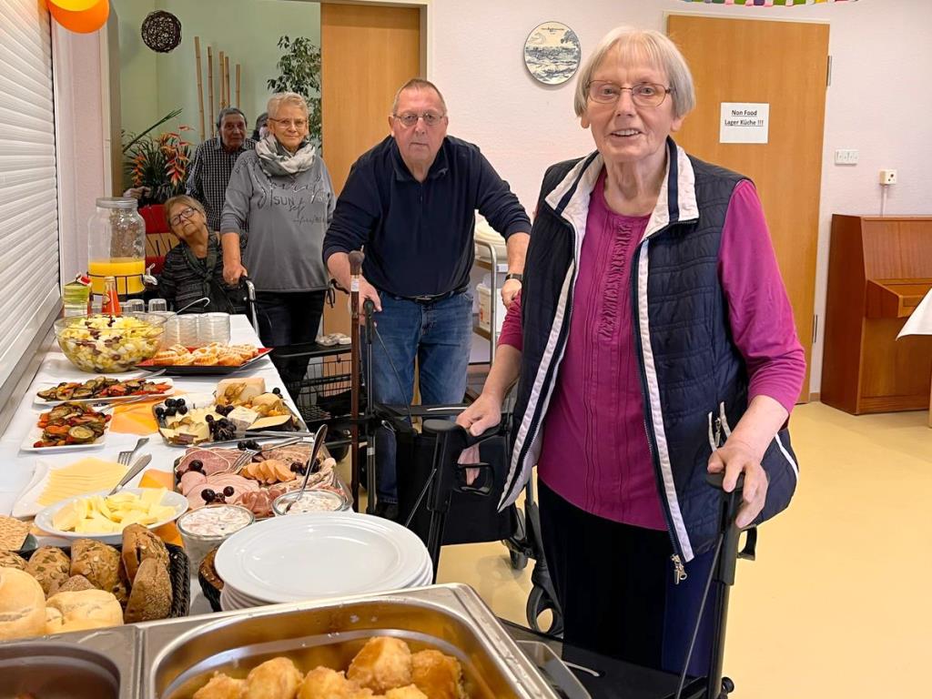 Eine Gruppe von älteren Menschen vor einem Buffet in einem Gemeinschaftsraum.