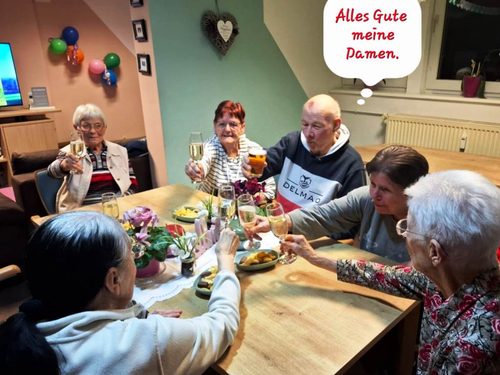 Eine Gruppe von Senioren sitzt um einen Tisch und stoßt mit Sekt an.