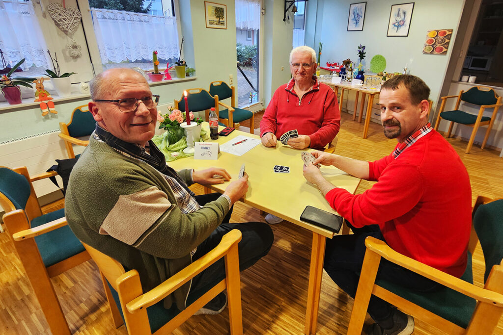 Drei M&auml;nner spielen Karten an einem Tisch.