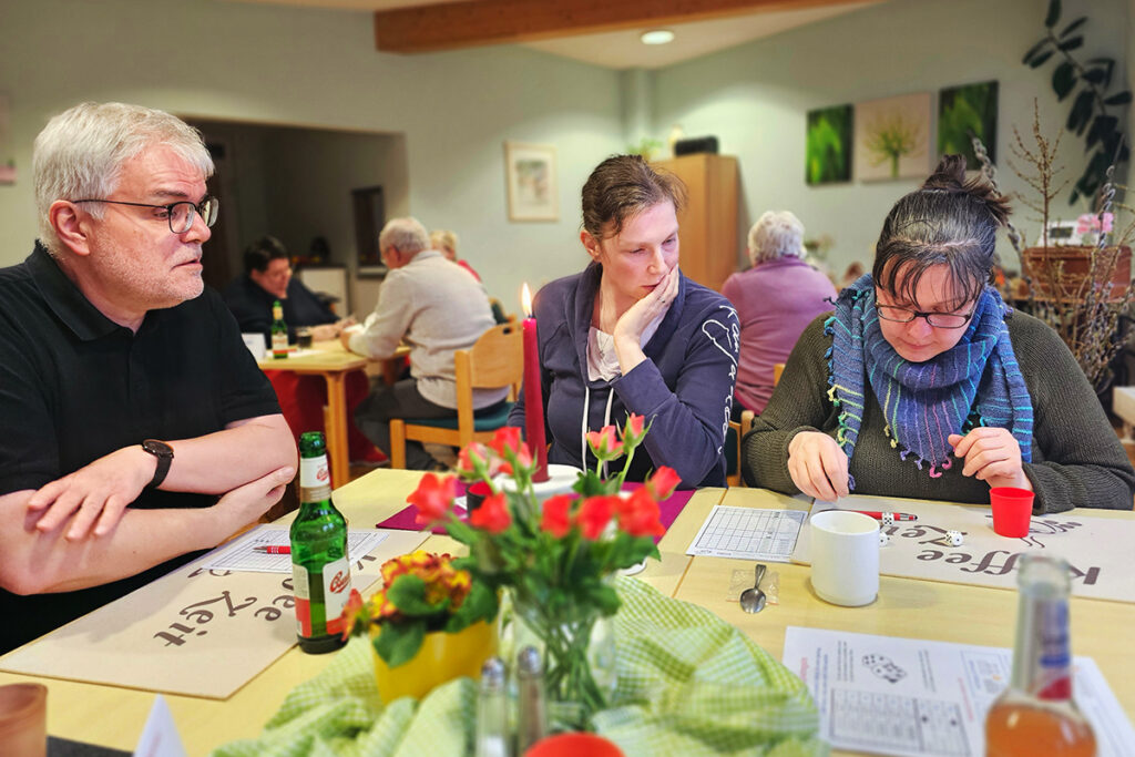 Menschen sitzen an einem Tisch in einem Gemeinschaftsraum mit Brettspiel.