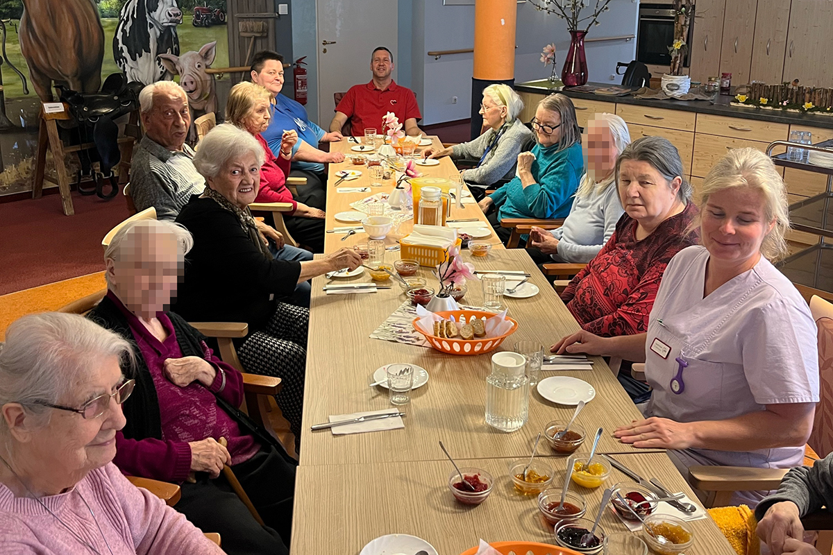 Eine Gruppe von Senioren und Pflegekräften sitzen um einen langen Esstisch.