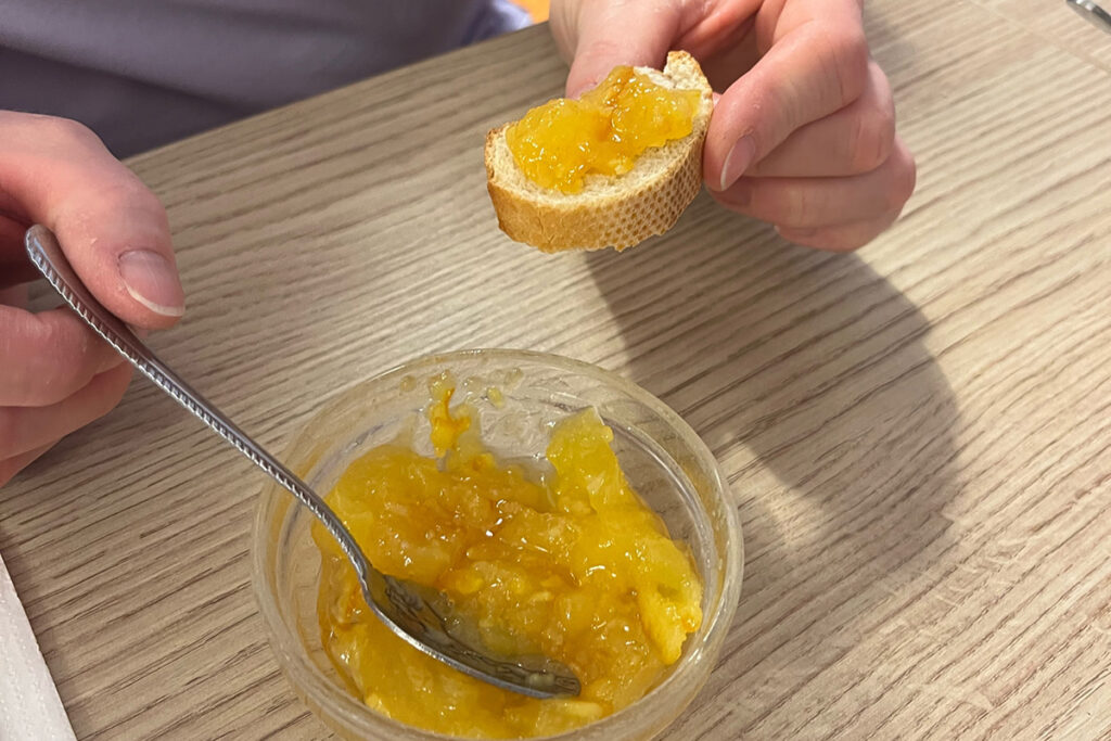 Eine Person h&auml;lt ein St&uuml;ck Brot mit Marmelade. Auf dem Tisch steht eine Schale mit weiterer Marmelade und einem L&ouml;ffel.