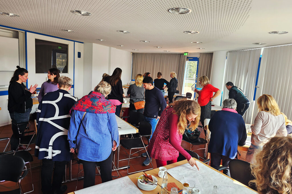 Gruppen von Menschen arbeiten zusammen in einem Konferenzraum mit gro&szlig;en Tischen und Papier auf den Tischen.