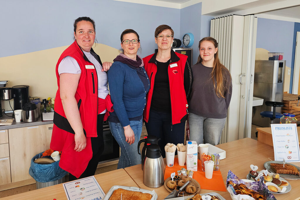 Vier Personen stehen hinter einem Tisch mit Speisen und Getr&auml;nken.