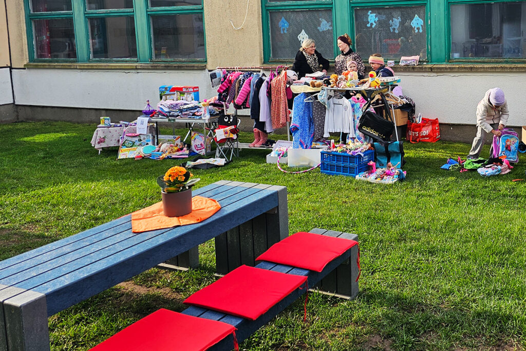 Flohmarkt im Freien vor einem Geb&auml;ude mit gr&uuml;nen Fenstern.