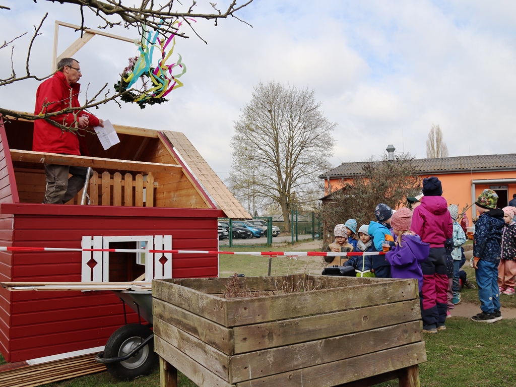 Ein Mann auf einem rot gestrichenen Karrenhaus spricht zu einer Gruppe von Kindern.