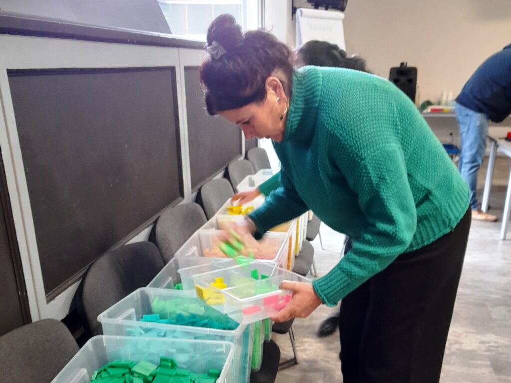 Eine Person sortiert bunte Plastikbausteine in durchsichtigen Boxen.