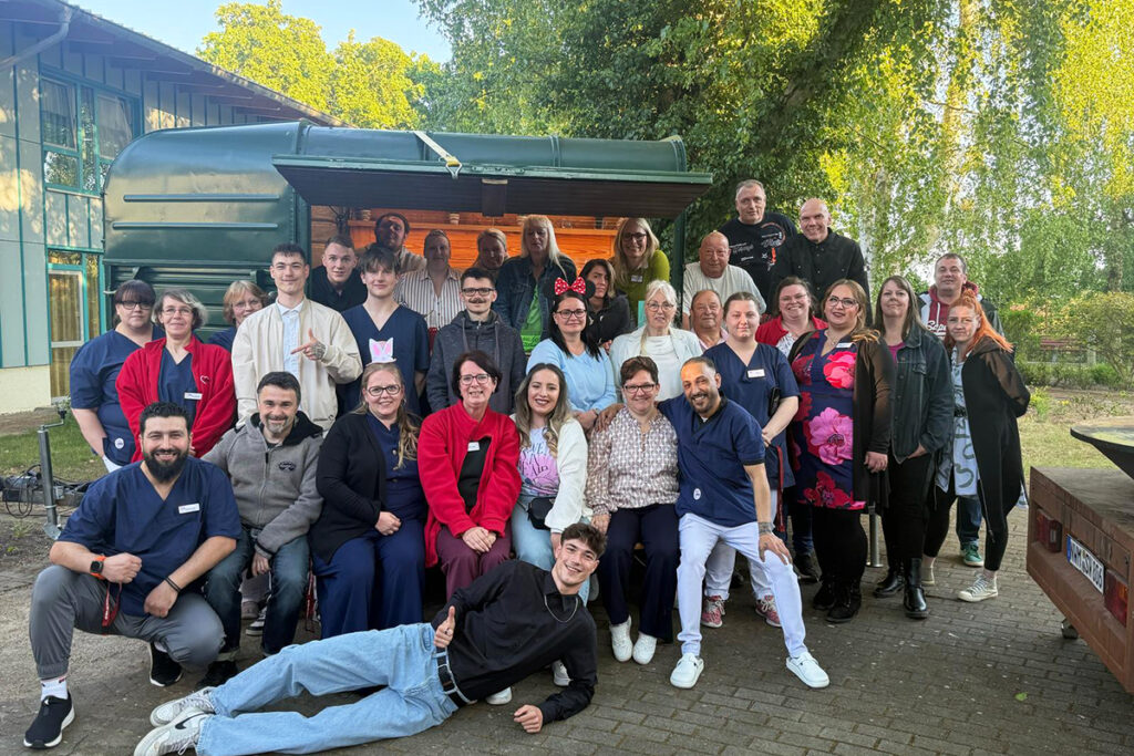 Gruppe von AWO-Mitarbeiter*innen posiert f&uuml;r ein Foto im Freien vor einem gr&uuml;nen Geb&auml;ude.