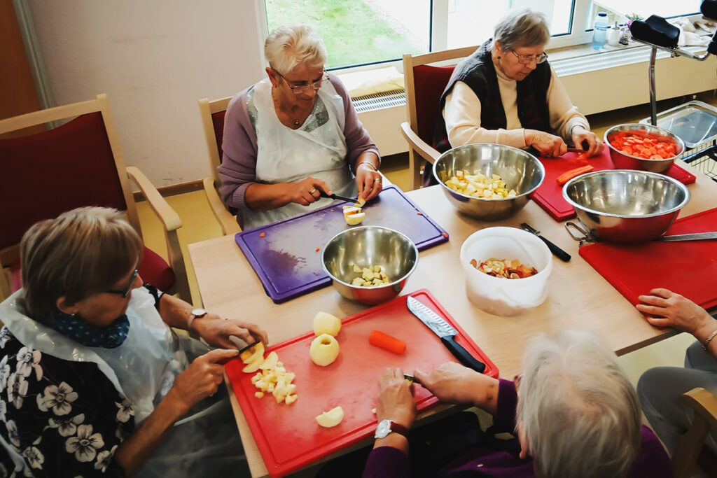 &Auml;ltere Frauen schneiden Obst und Gem&uuml;se an einem Tisch.