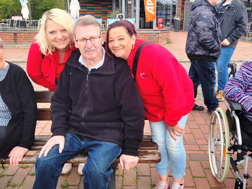 Gruppenfoto mit AWO-Mitarbeiterinnen und älterem Mann auf einer Bank.