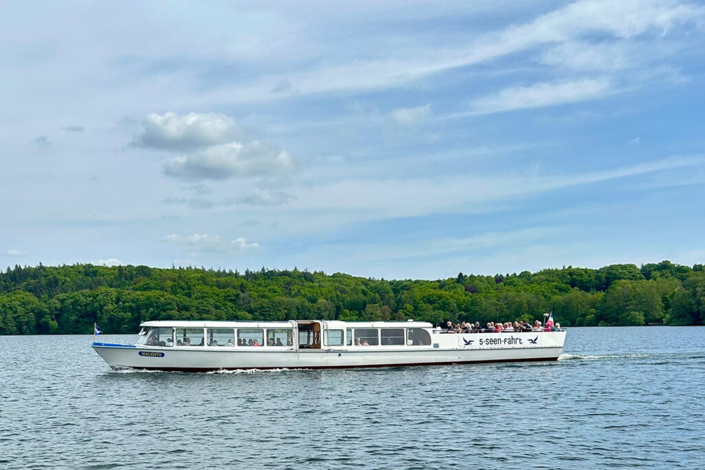 Ein Boot mit der Aufschrift '5-Seen-Fahrt' auf einem See, im Hintergrund B&auml;ume.