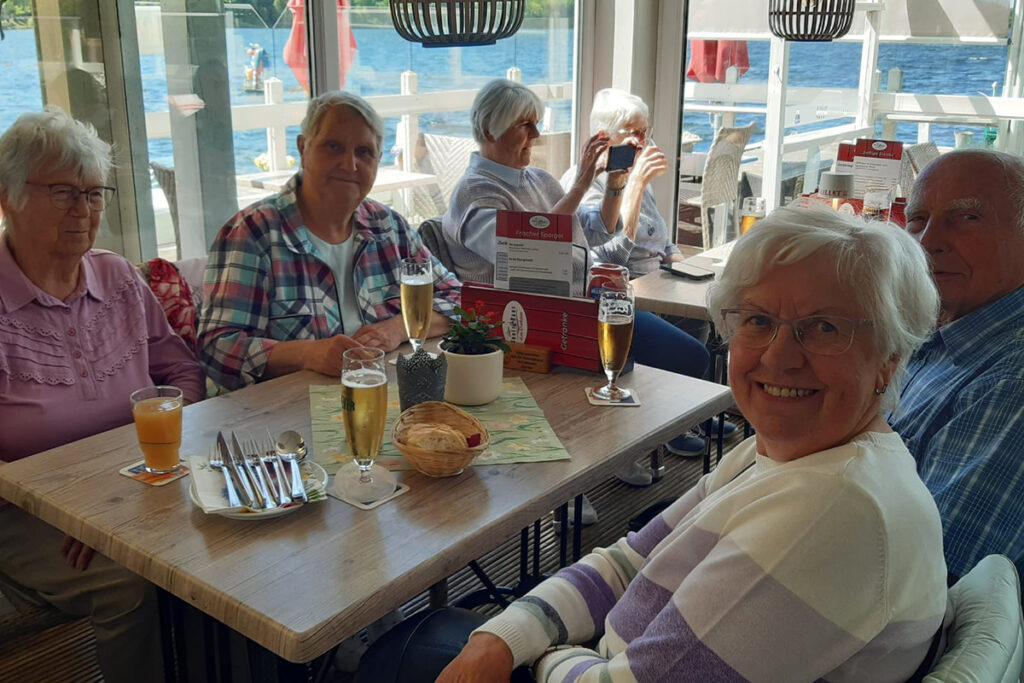 Eine Gruppe &auml;lterer Menschen in einem Caf&eacute; mit Blick auf einen See.