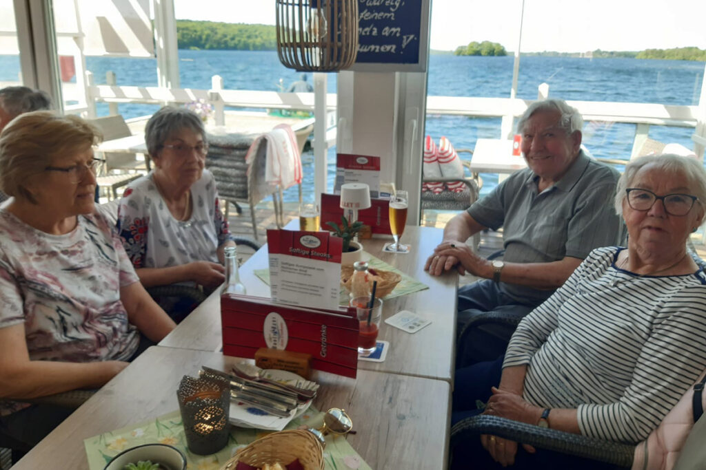 Eine Gruppe &auml;lterer Menschen sitzt an einem Tisch in einem Restaurant mit Blick auf einen See.