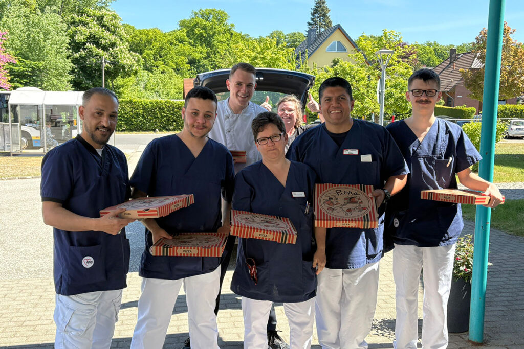Eine Gruppe von Menschen in blauer Berufskleidung, die Pizza-Schachteln halten.