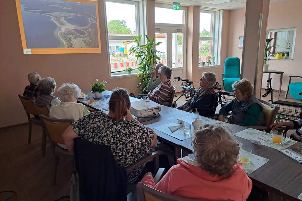 Seniorengruppe in einem Raum, die sich eine Projektion ansieht.