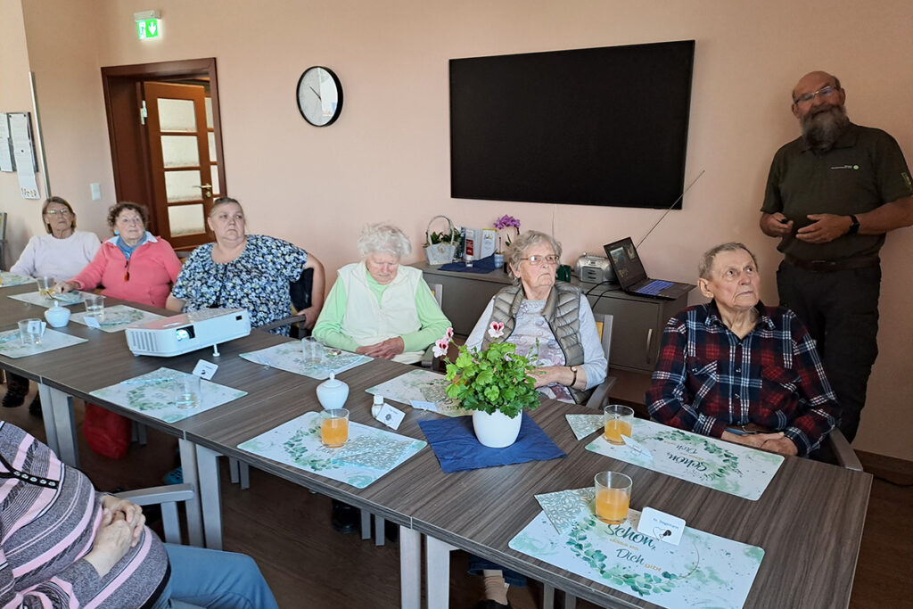Menschen w&auml;hrend einer Pr&auml;sentation in einem Raum mit Tisch und St&uuml;hlen.