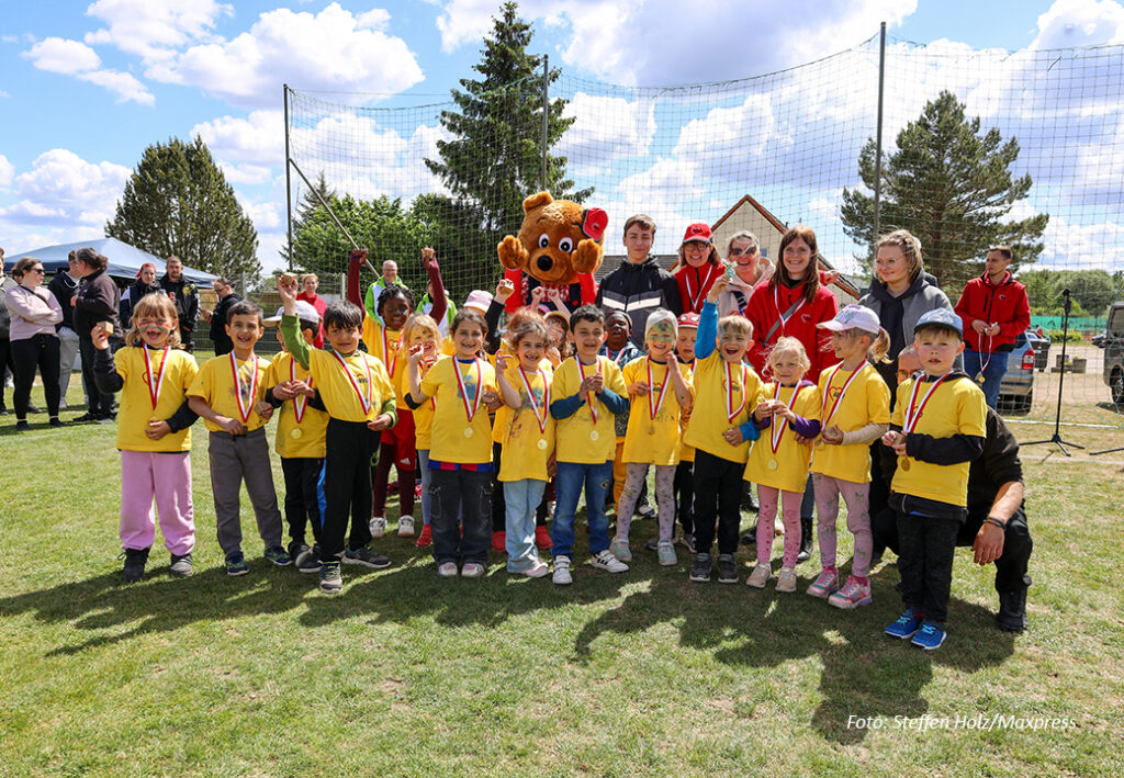 Gruppe von Kindern mit gelben T-Shirts und Medaillen sowie Erwachsene in roter Kleidung
