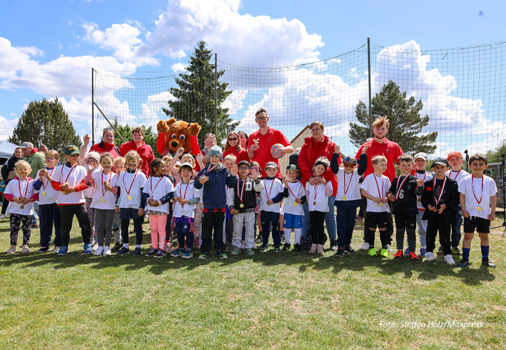 Gruppe von Kindern und Erwachsenen auf einem Sportplatz, einige tragen Medaillen.