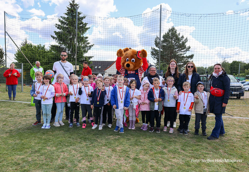 Gruppe von Kindern mit Medaillen und Erwachsenen im Freien vor einem Fu&szlig;ballnetz.