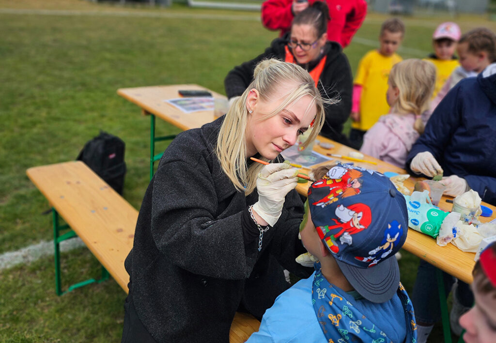 Eine Frau bemalt ein Kindergesicht bei einem Outdoor-Event.