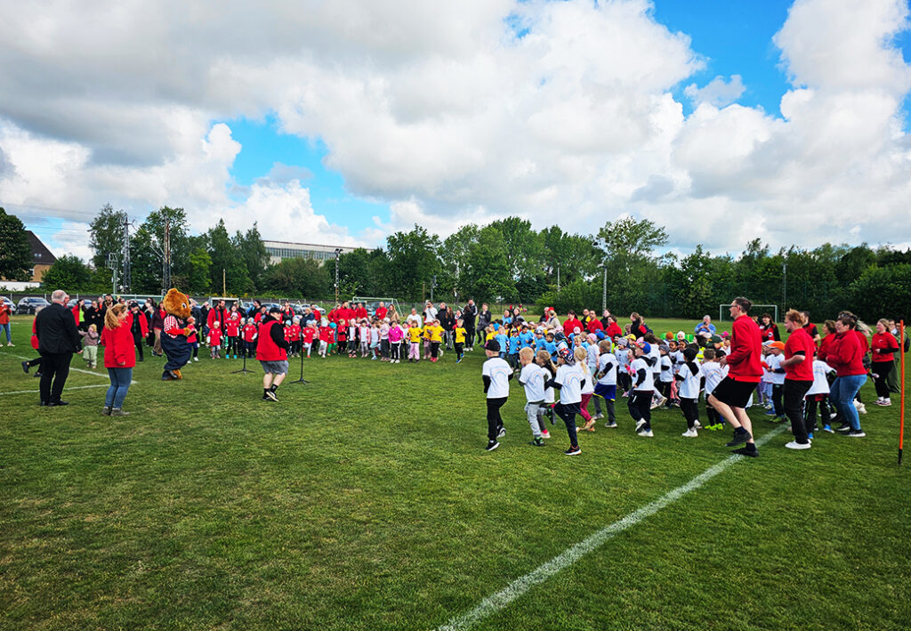 Viele Kinder und Erwachsene versammelt auf einem Fu&szlig;ballfeld