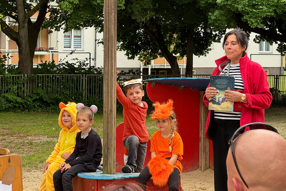Kinder in Tierkostümen sitzen draußen auf einem Spielplatz.