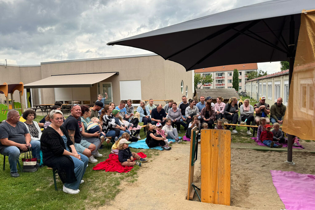 Eine Gruppe von Erwachsenen und Kindern sitzt drau&szlig;en in einem Hof.