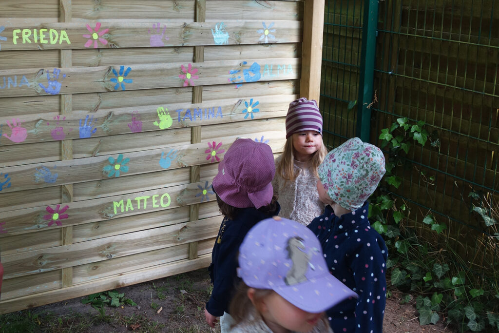 Kinder vor einer bemalten Holzwand