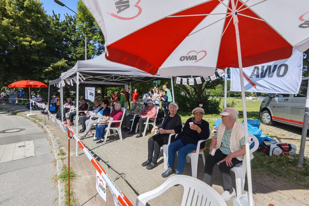 Gruppe von Menschen sitzt unter AWO-Sonnenschirmen bei einer Veranstaltung.