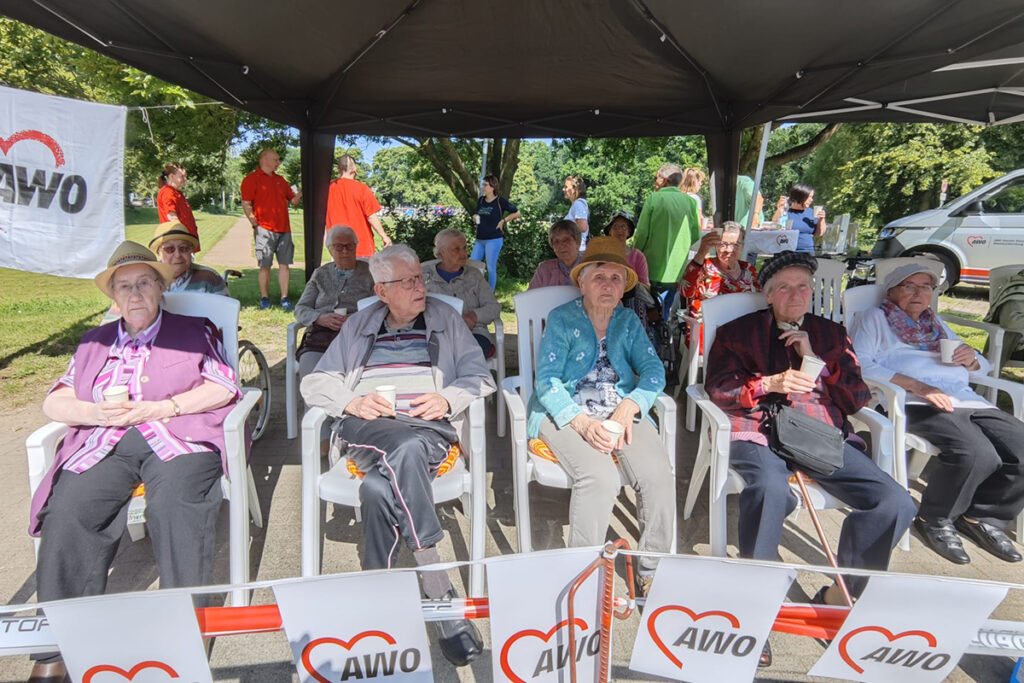 &Auml;ltere Menschen in einem Zelt, umgeben von AWO-Logo-Bannern.