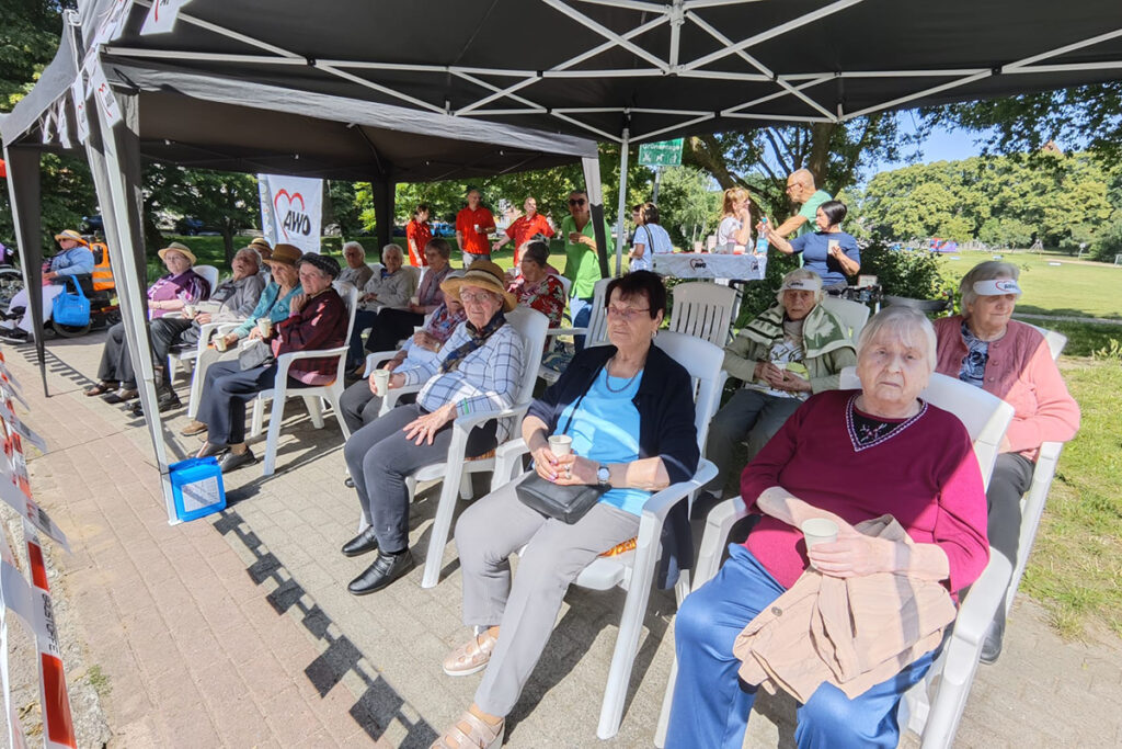 Eine Gruppe von Senioren sitzt unter einem schattenspendenden Pavillon.