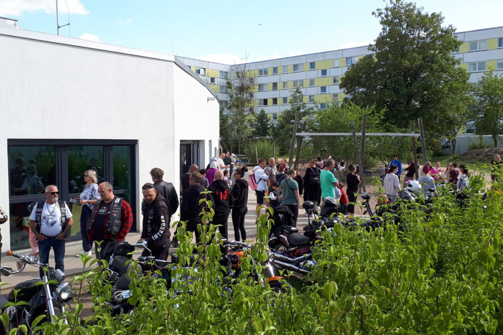Gruppe von Menschen vor einem Geb&auml;ude mit Motorr&auml;dern im Vordergrund