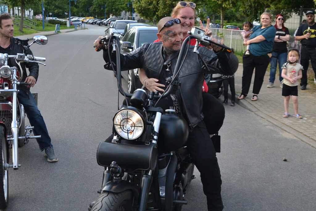 Zwei Menschen auf einem Motorrad bei einer Veranstaltung im Freien.