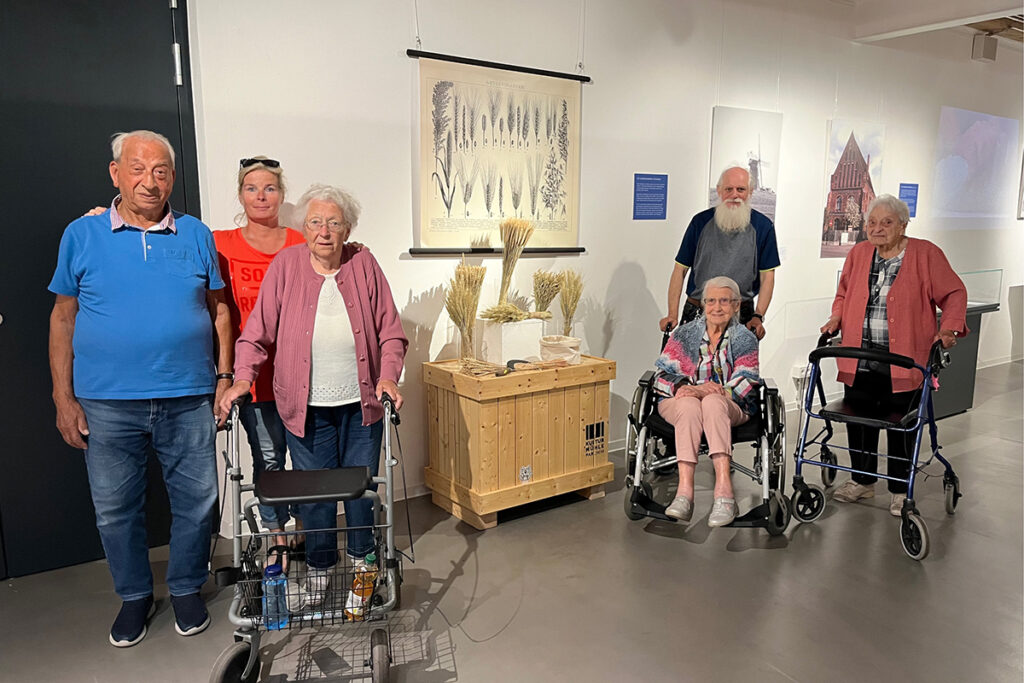 Eine Gruppe von sechs Senioren, einige mit Rollatoren oder im Rollstuhl, steht in einem Ausstellungsraum.
