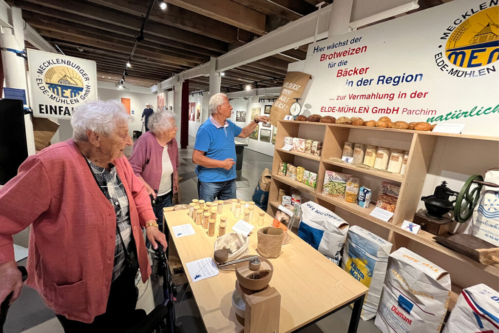 Drei Personen betrachten eine Ausstellung &uuml;ber Getreide und Mehl