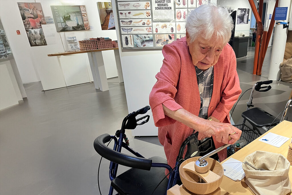 &Auml;ltere Frau interagiert mit einer Ausstellung in einem Museum