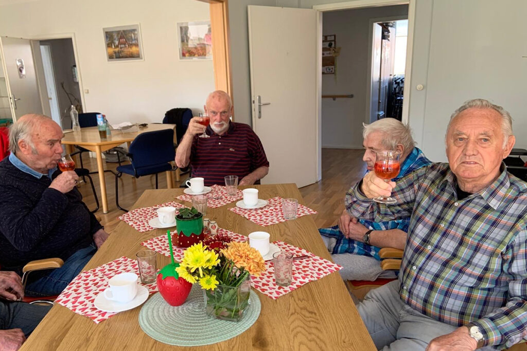 Eine Gruppe älterer Menschen sitzt an einem Tisch und hebt Gläser mit Getränken.