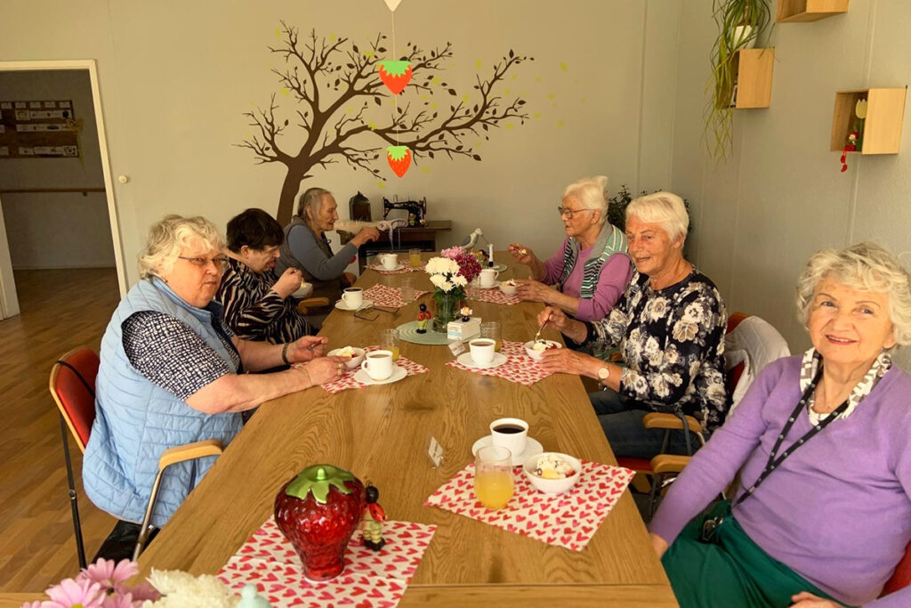 Eine Gruppe &auml;lterer Menschen sitzt l&auml;chelnd an einem Tisch und genie&szlig;t eine Mahlzeit.