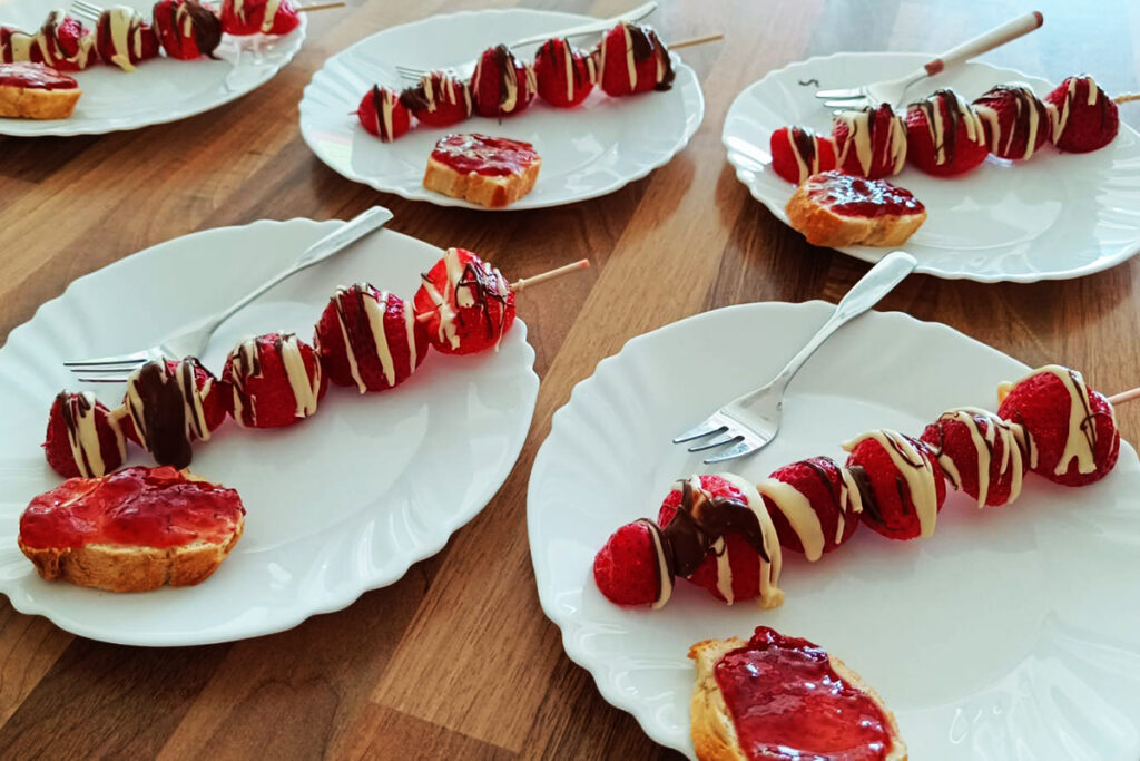 Teller mit Erdbeerspie&szlig;en und Brot mit Marmelade auf Holztisch
